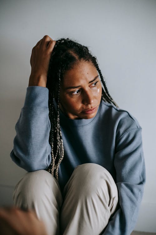 Free Mournful nervous African American female in casual wear crying on floor while embracing knees and looking away Stock Photo