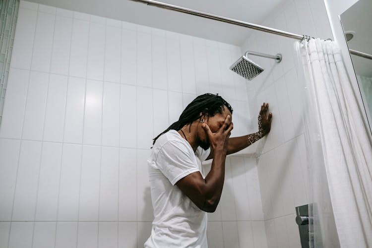 Stressed Black Man Covering Face With Hand In Shower