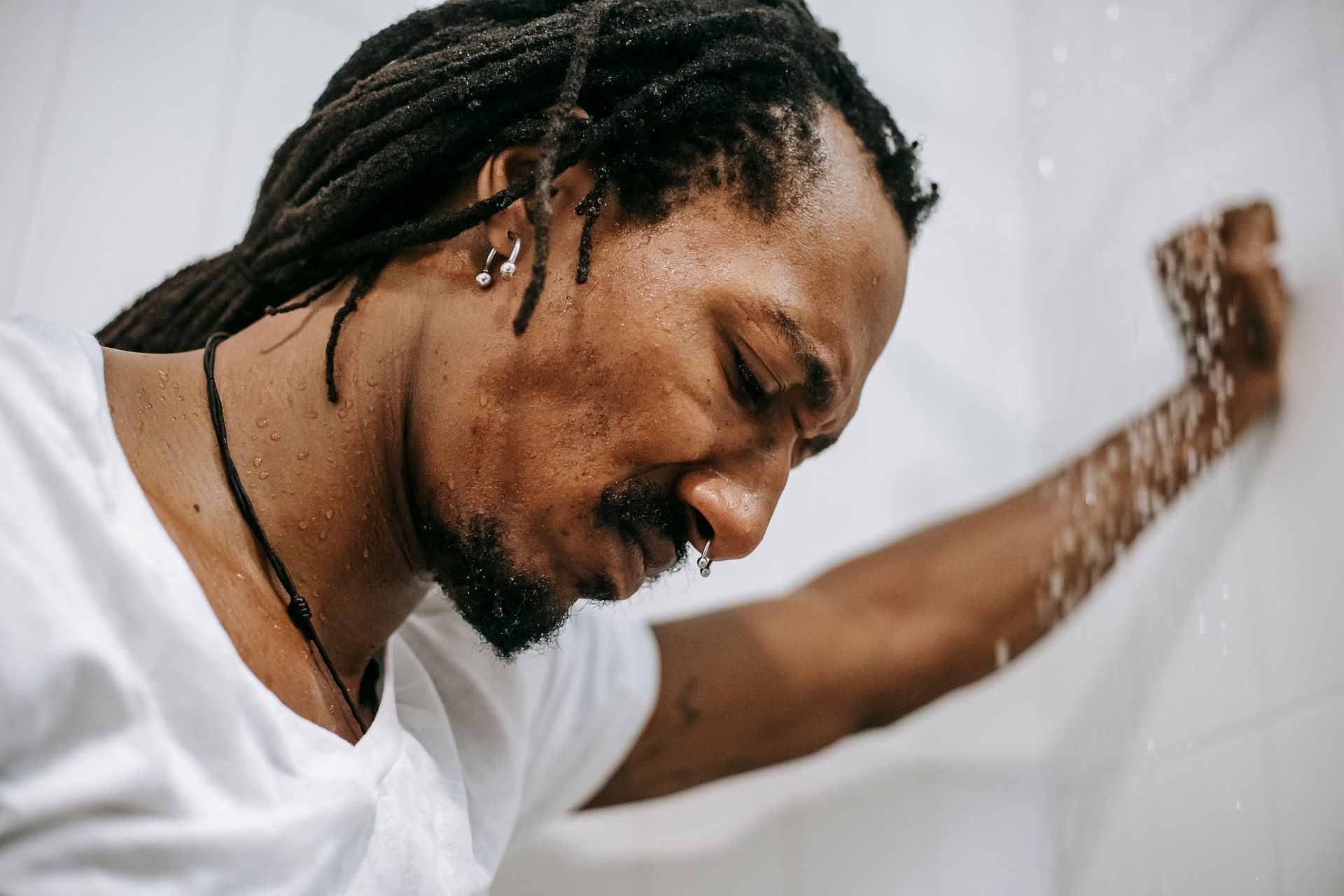 Crop irritated uncertain African American male in white short standing in shower cabin and frowning in dismay
