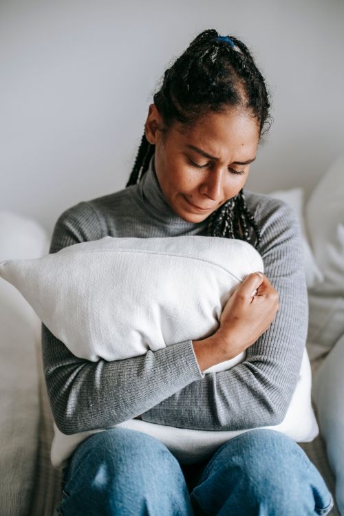 Free Overwhelmed helpless African American female in casual wear hugging pillow and crying hopelessly in bedroom Stock Photo