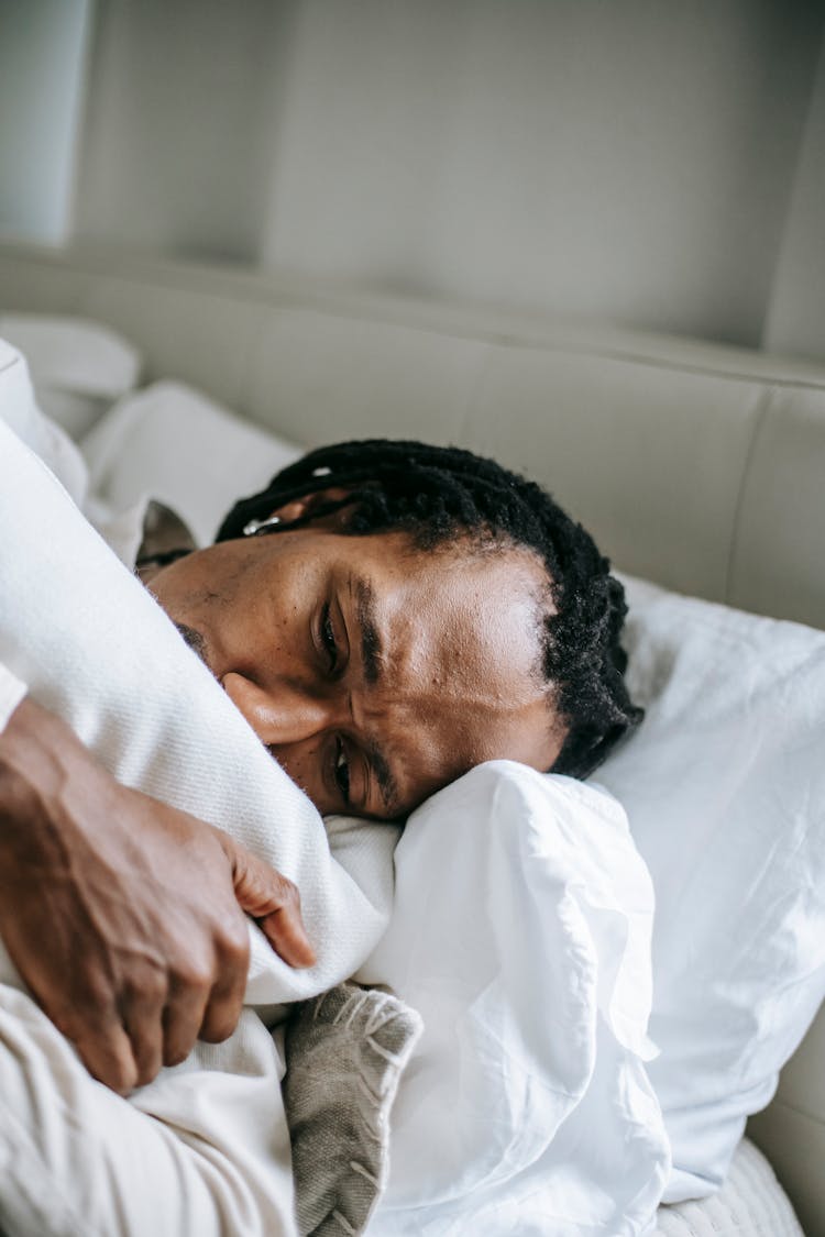 Uncertain Stressed Black Man Hugging Pillow On Bed