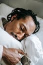 From above pondering stressed African American male hugging pillow and looking away in sad thoughts while lying on bed