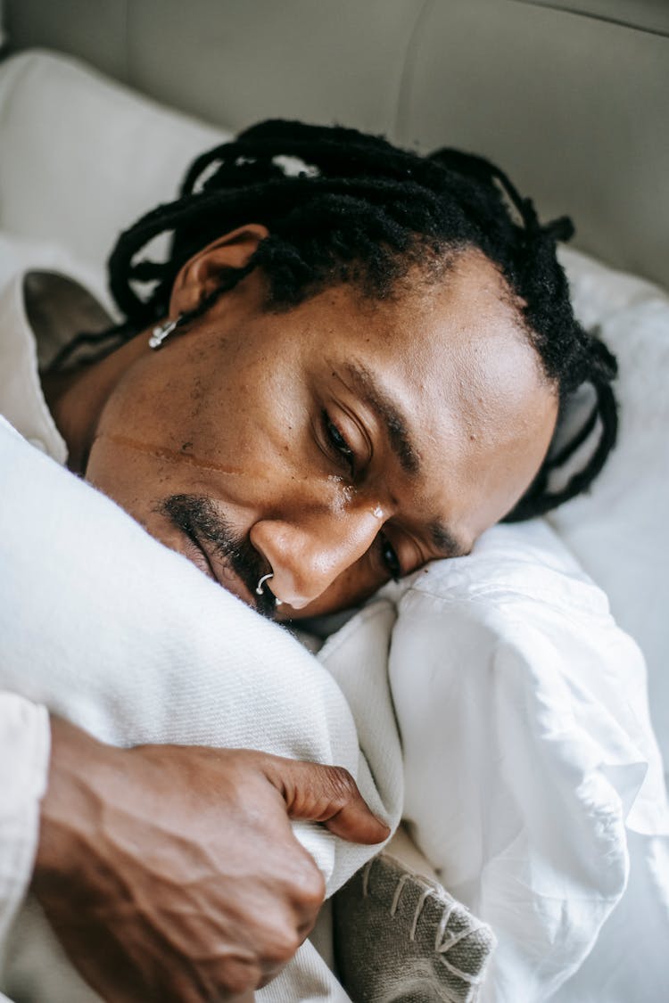 Concerned Black Man Hugging Pillow On Bed