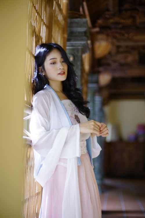 Free Side view of charming native Asian woman with black hair in white outfit standing near wall of traditional building with columns Stock Photo