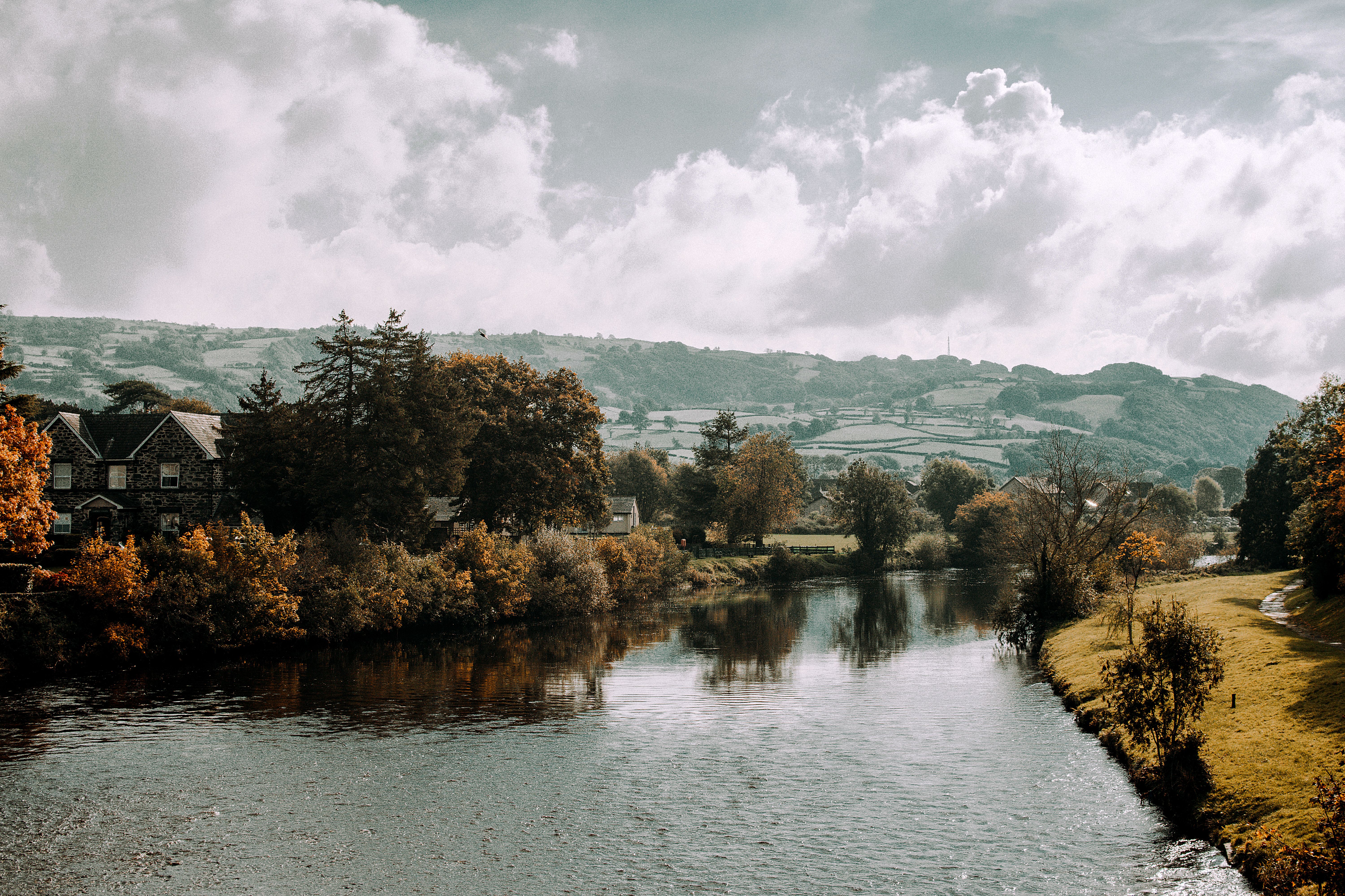Picturesque autumn view of a river in Llanrwst, Wales with lush greenery and dramatic clouds.