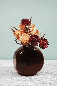 蓝色背景下，干花在棕色陶瓷花瓶中的排列十分美观