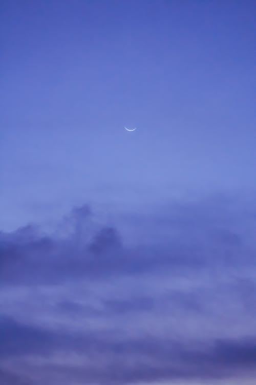 Free Crescent moon Earth natural satellite shining on blue sky with dark clouds in evening Stock Photo