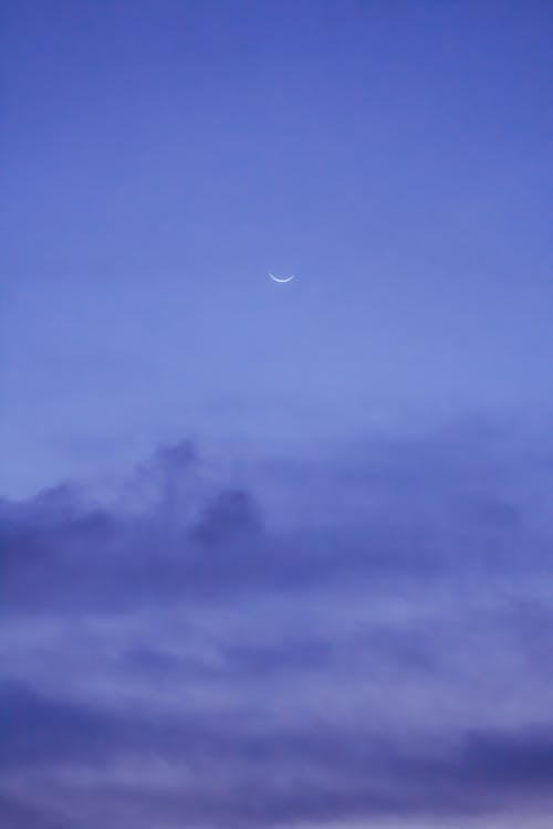 Crescent moon Earth natural satellite shining on blue sky with dark clouds in evening