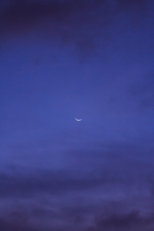 Dark clouds floating on blue sky with shining crescent moon in evening in nature