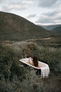 一位女士在风景优美的山脉背景下，于僻静的户外浴缸中享受轻松的沐浴