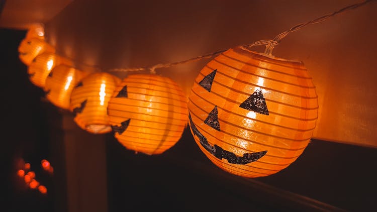 A Halloween Pumpkins With Lights Hanging Near The Wall