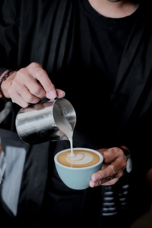 A Person Pouring Milk Foam on Coffee