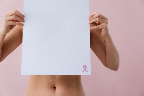Free Image of a woman holding a blank paper with pink ribbon for breast cancer awareness. Stock Photo