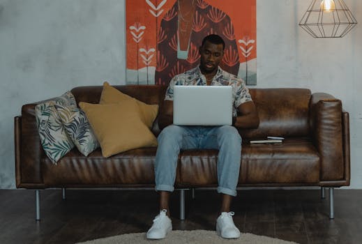 A man sitting on a sofa using his laptop within a stylish living room setting, embodying modern home lifestyle.