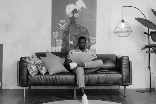 Black and white photo of a man working remotely on a laptop in a stylish indoor setting.