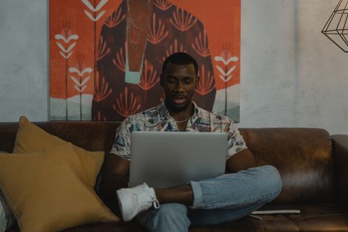 Free Man sitting on leather sofa using laptop for work in a cozy home setting. Stock Photo