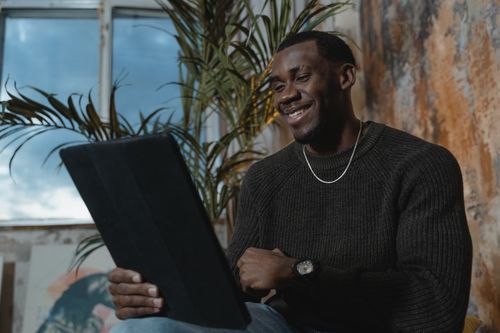 Free Smiling man in a knit sweater on a cozy indoor video call using a tablet. Stock Photo
