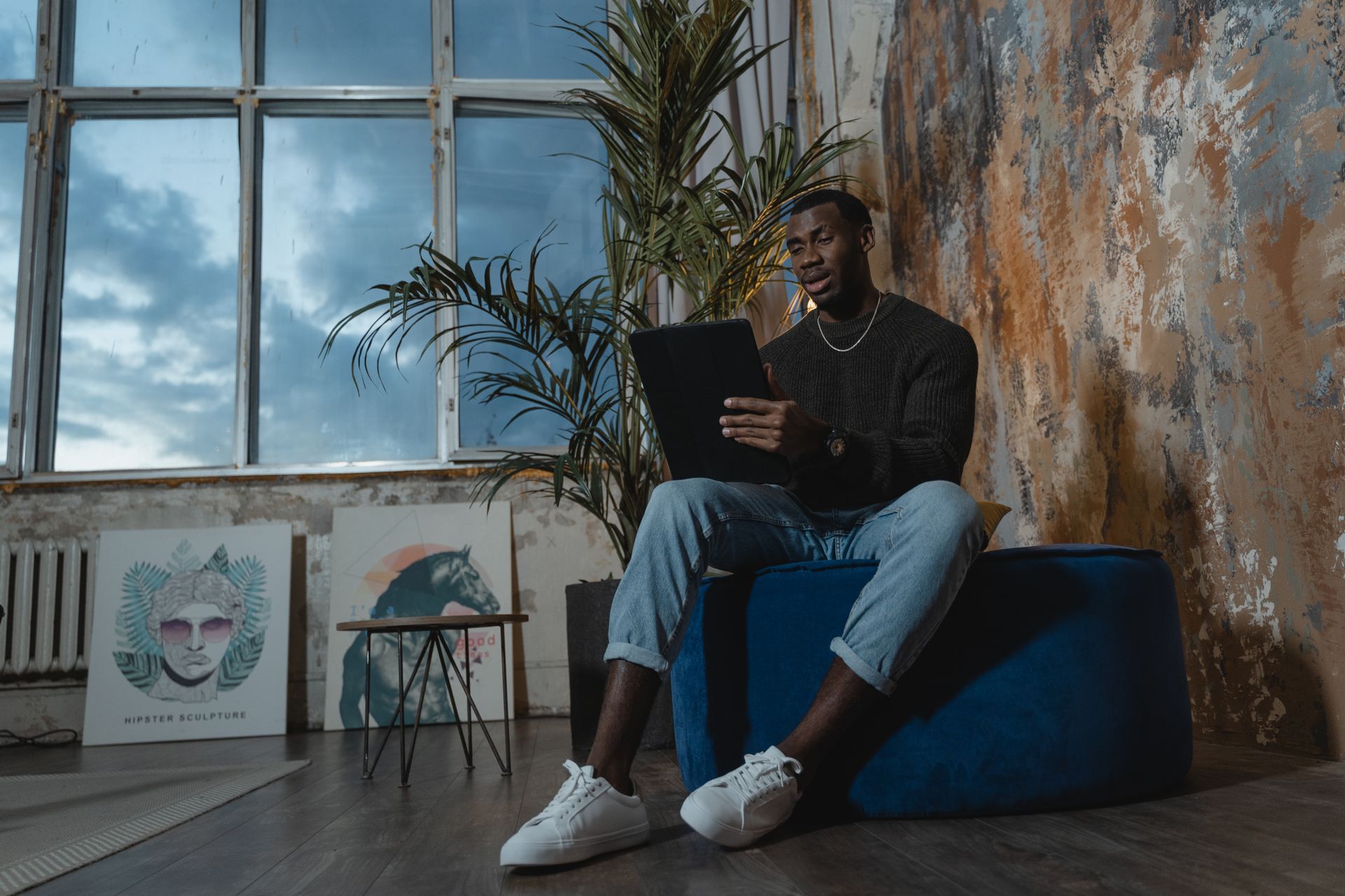 African American man making a video call on a tablet while sitting indoors in a modern, artistic setting.