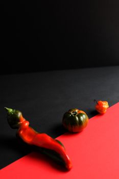 Dramatic close-up of peppers and tomato on a red and black background, showcasing vibrant colors and artistic composition.