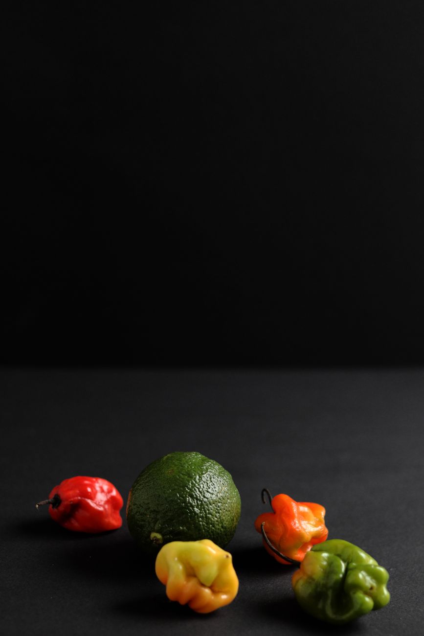 Fresh scotch bonnet peppers alongside grains of paradise, dried locust beans, and other West African spices arranged on a rustic wooden cutting board