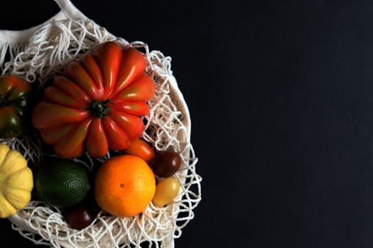 Colorful assortment of fresh vegetables and fruits in a reusable net bag against a black background.