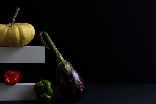A creative display of eggplant, pumpkin, and peppers on a dark background.