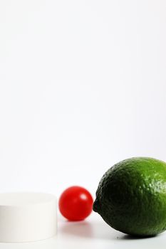 A minimalist close-up of a lime and cherry tomato on a white background.