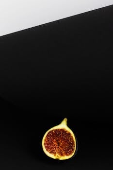 Slice of ripe fig on black background, showcasing minimalist still life photography.