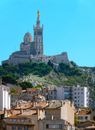 Ancient palace with dome and tower located on top of grassy hill near buildings placed at foothill against blue sky