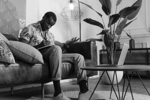 African American man working from home in a stylish living room with laptop and plants.