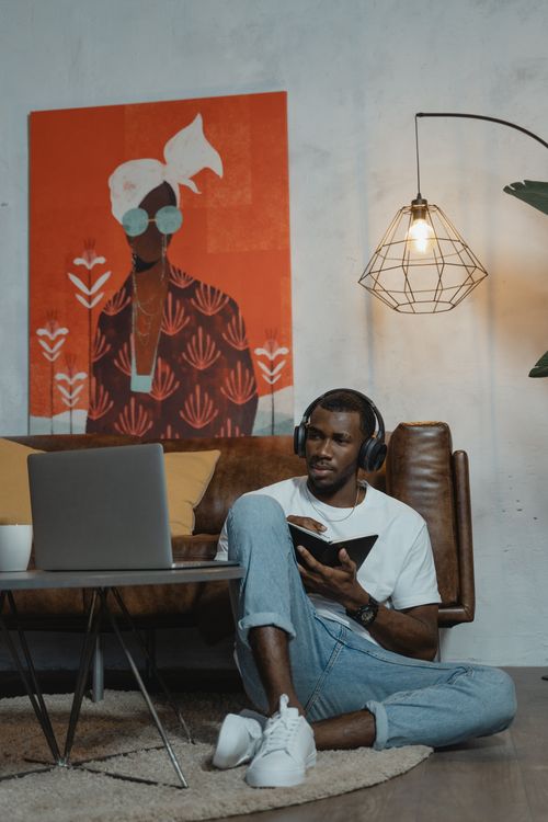 Free A young African American man studies online from his living room, using a laptop and notebook. Stock Photo