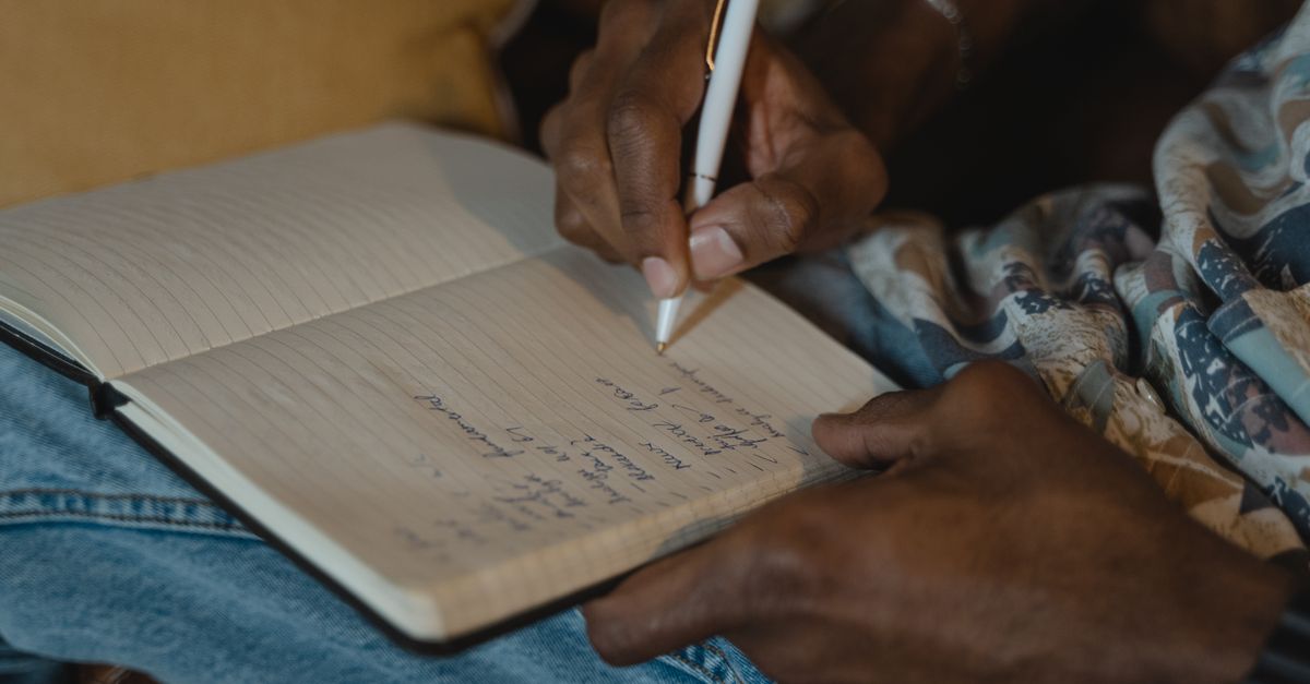 A detailed close-up of hand writing notes in a lined notebook using a white pen indoors.