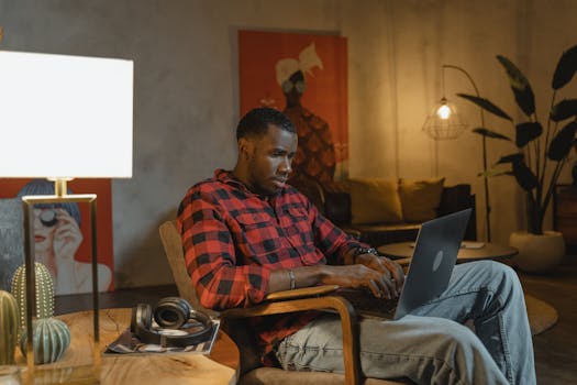 Adult Black man focused on remote work with a laptop in a cozy, stylish home setting.