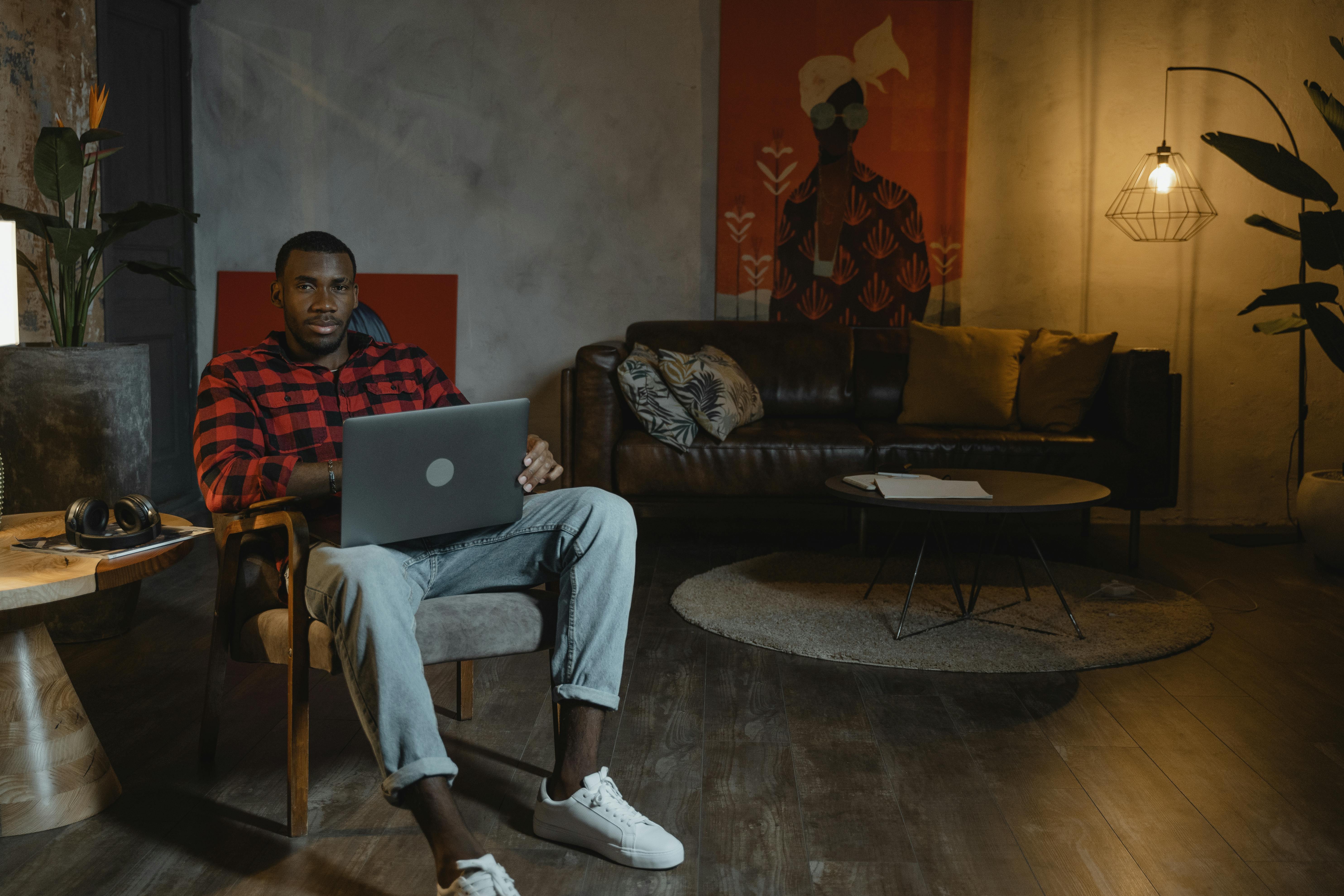 man in red and black checkered dress shirt sitting on couch using macbook