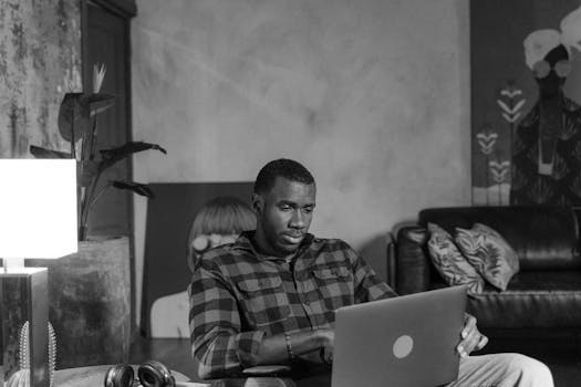 African American man concentrating on laptop work in a cozy, artistic home setting.