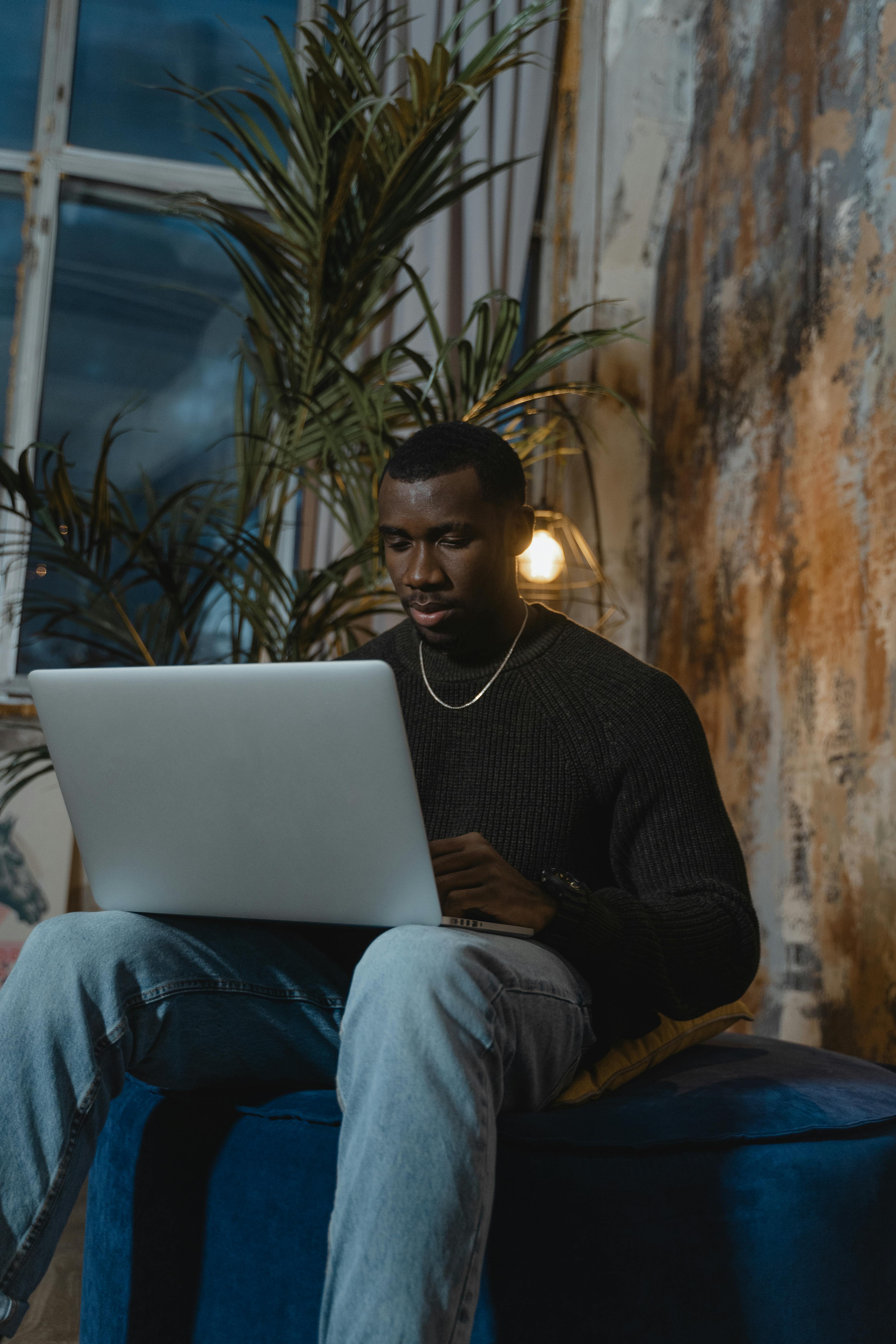 man in black sweater sitting on couch using laptop