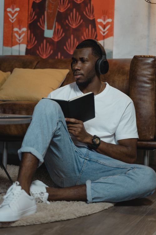 Free African American man learning online, sitting with headphones and notebook indoors. Stock Photo