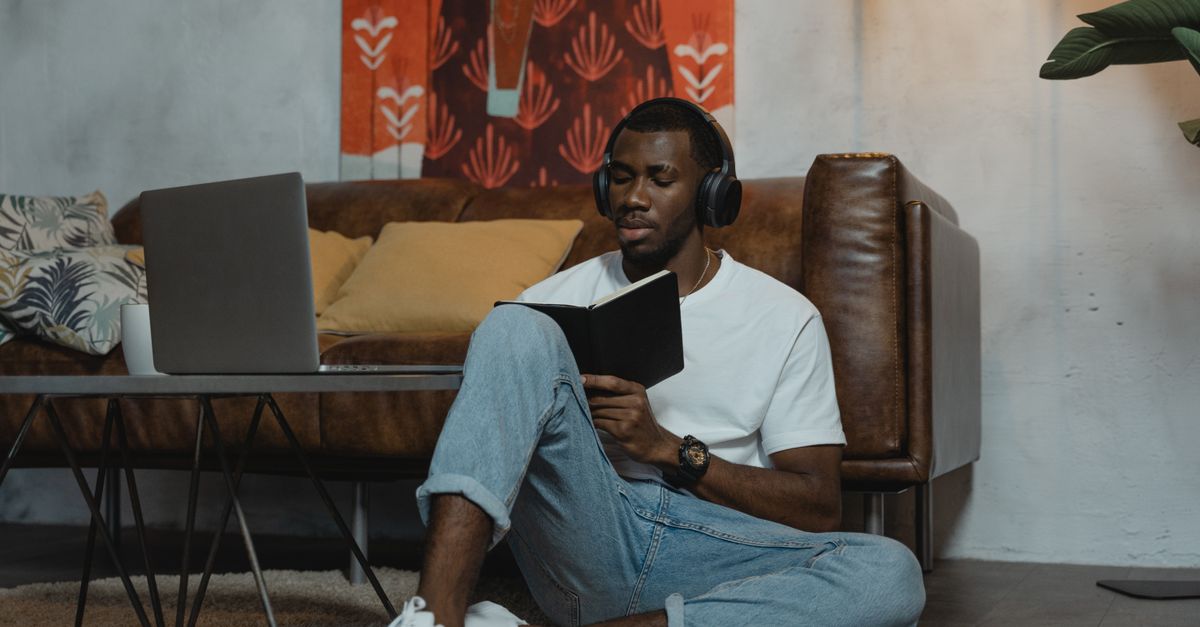 A man wearing headphones studies on the floor with a laptop nearby, embracing modern online education.
