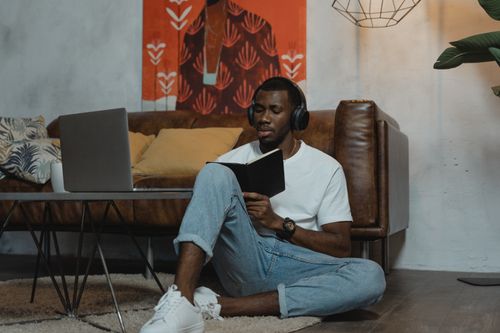 Free A man wearing headphones studies on the floor with a laptop nearby, embracing modern online education. Stock Photo