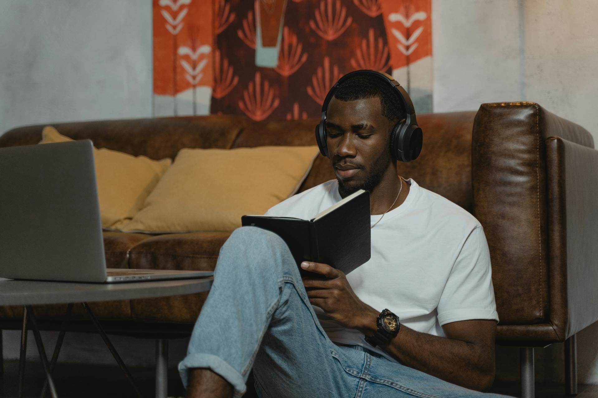 Focused young adult using headphones and a notebook while studying online at home.