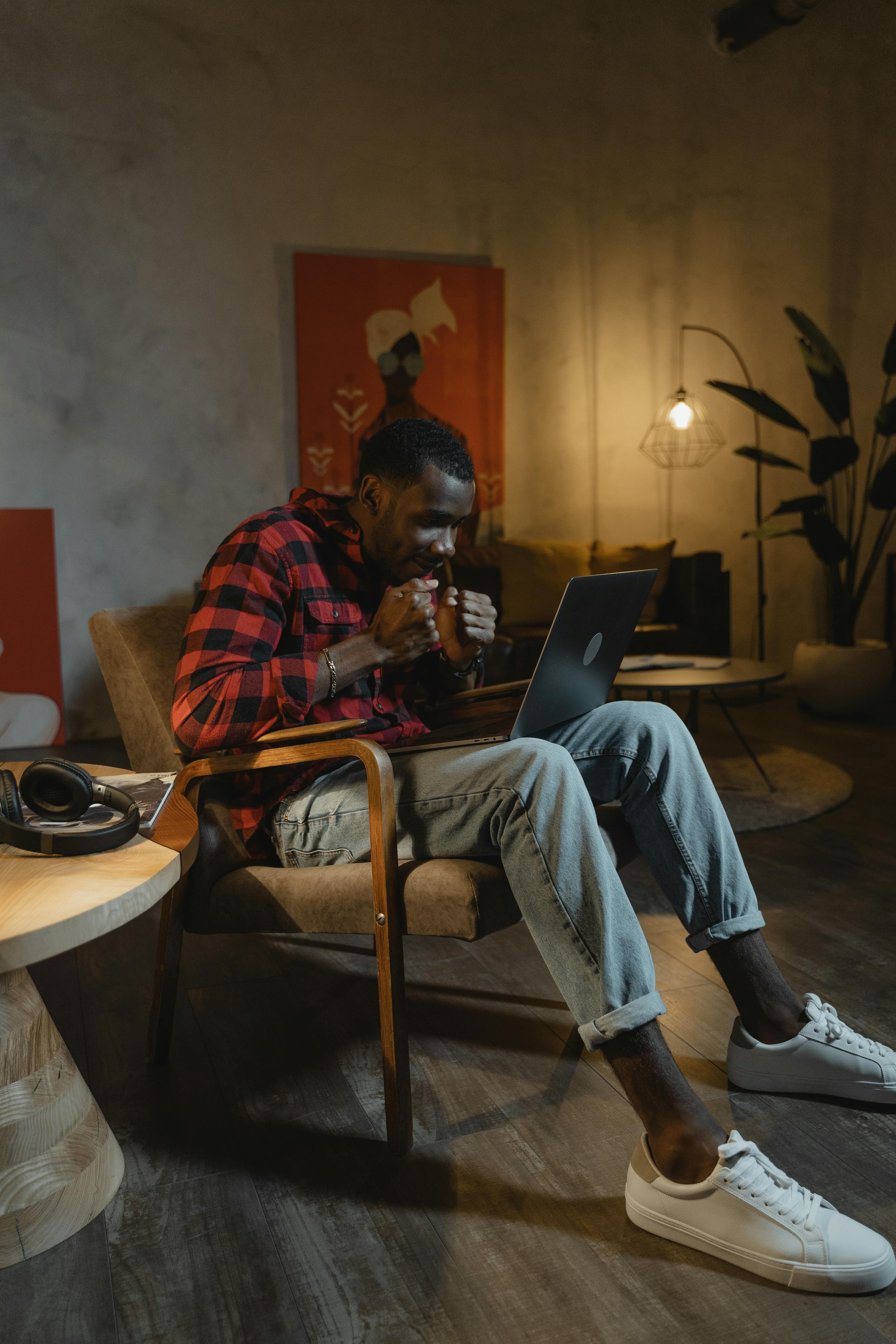 man in red and black plaid shirt and blue denim jeans sitting on chair using laptop