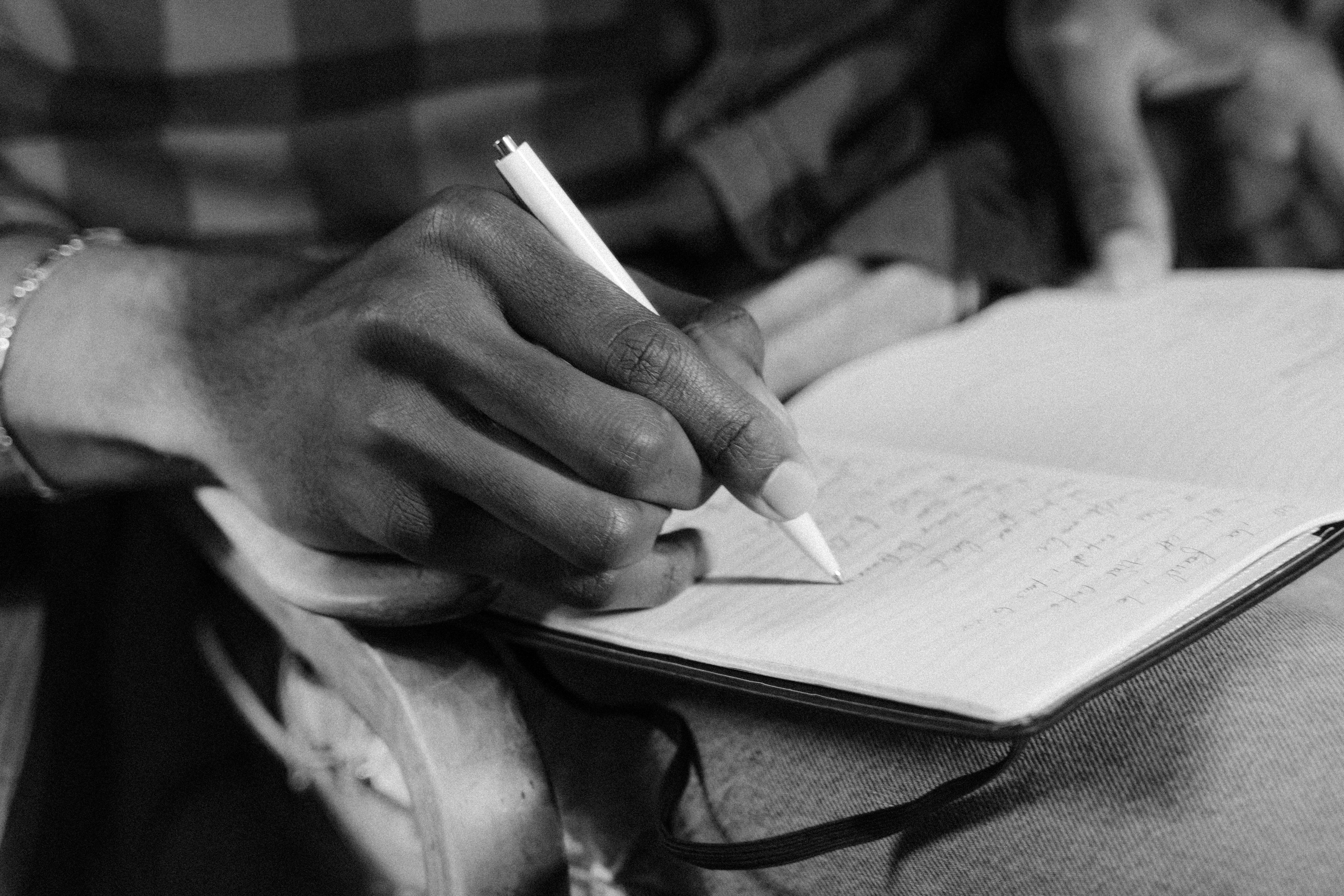 Grayscale Photo Of A Person Writing On Notebook · Free Stock Photo