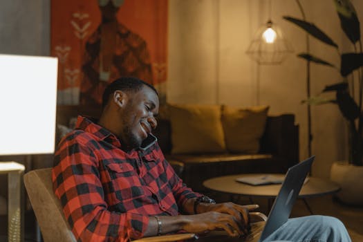 Man multitasking with phone and laptop in cozy home office setting.