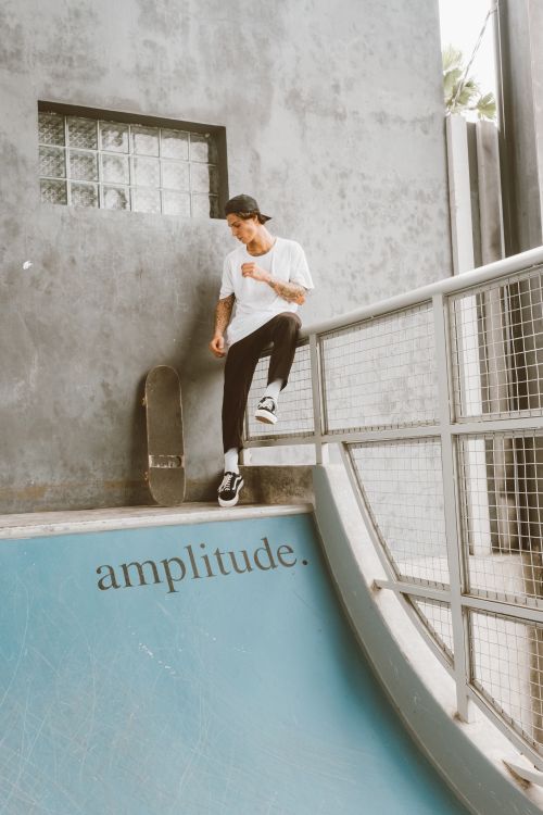 Free Casually dressed skateboarder relaxes by a ramp railing in an urban park. Stock Photo