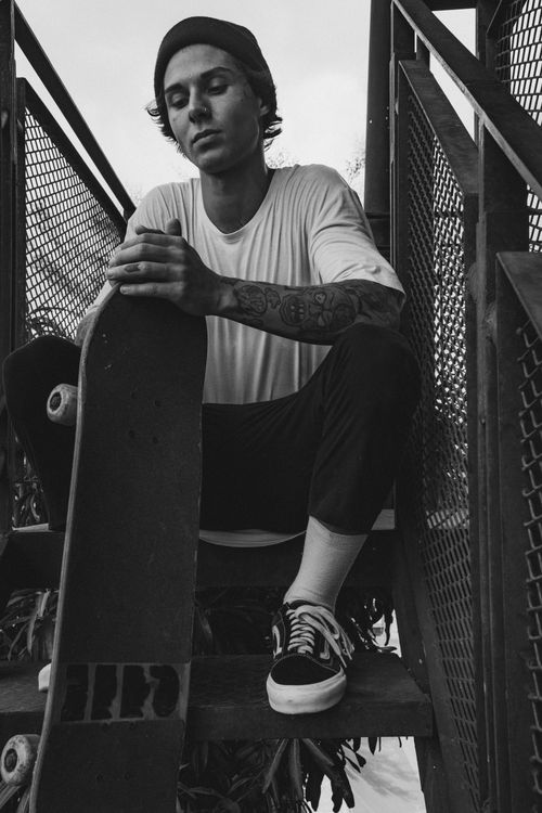 Free Monochrome photo of a skater sitting on stairs, holding a skateboard. Casual and introspective mood. Stock Photo