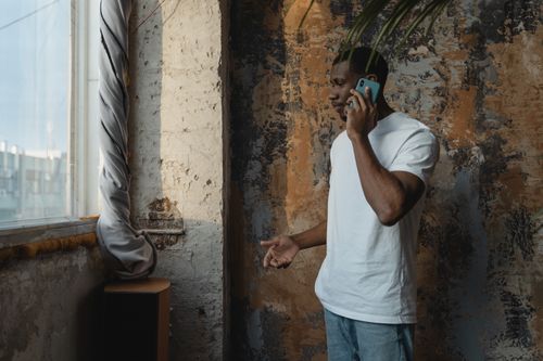 Free African American man in white shirt talking on a cellphone in an indoor setting. Stock Photo