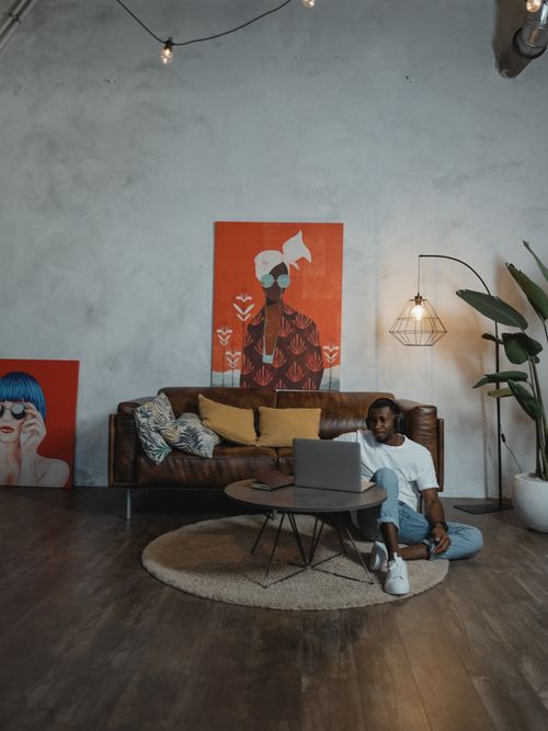 Free Man uses laptop in stylish living room for remote work or study, surrounded by modern decor. Stock Photo