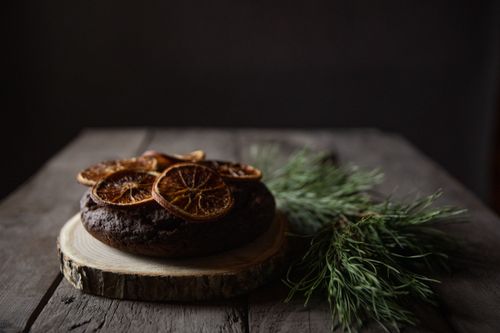 Free Dark, rustic gingerbread cake topped with dried orange slices on a wooden table with sprigs of pine. Stock Photo