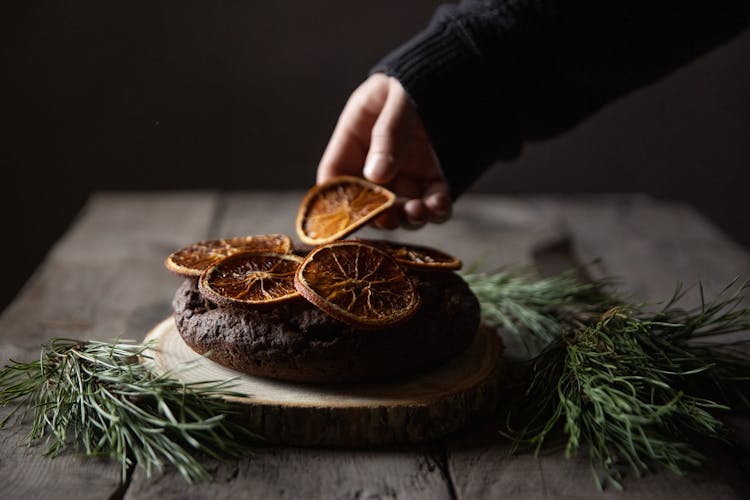 Person Decorating Chocolate Cake With Dried Orange Slices