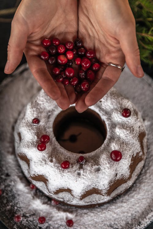 Person Holding Cranberries Near a Cake
